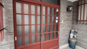 Uma porta de vidro vermelha com moldura de metal, um vaso azul com guarda-chuvas e um chão de azulejos.