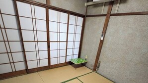Um espaço com tatames, um biombos shoji deslizante, uma pequena mesa verde e um ar condicionado instalado no teto.