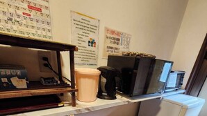 Cozinha compacta equipada com micro-ondas, máquina de café e frigorífico. Há também contentores de lixo e um calendário na parede.