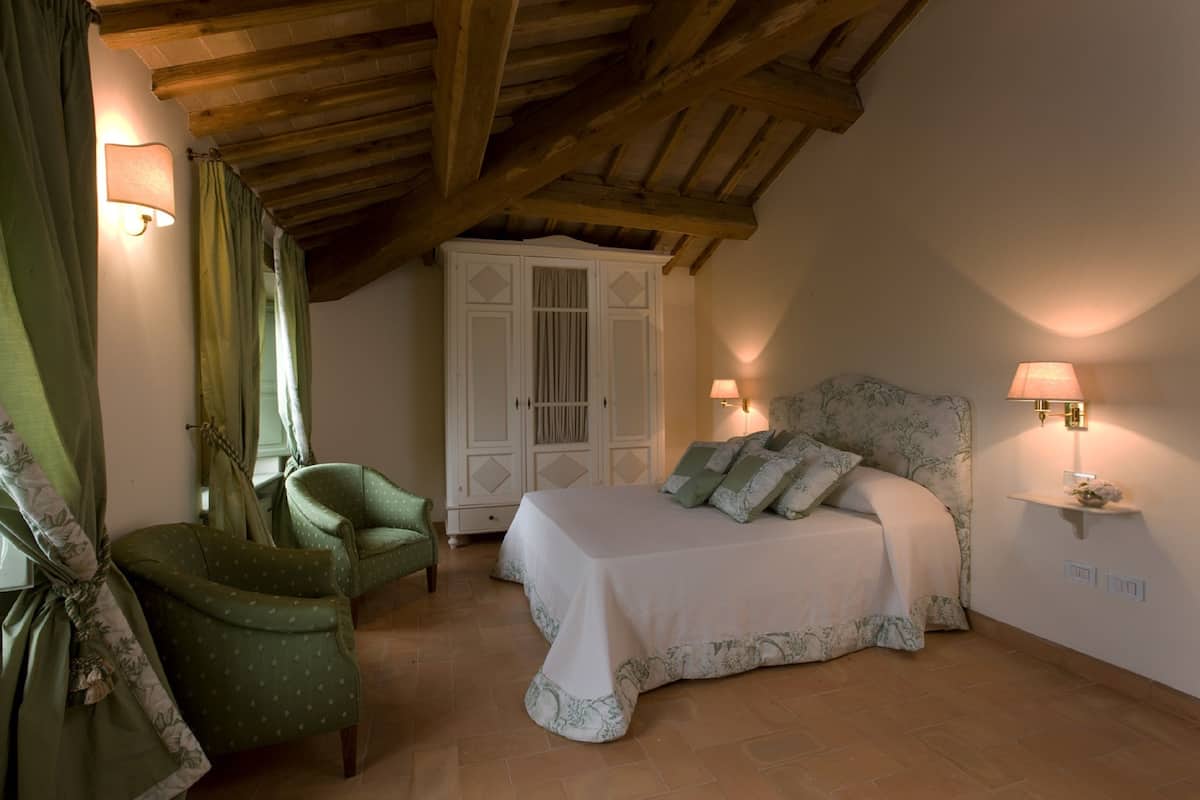 Een slaapkamer met een bed, twee stoelen, een kledingkast en wandlampen.