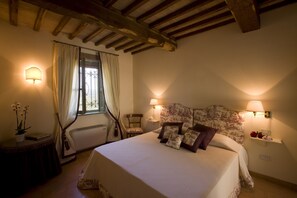 Une chambre avec un grand lit, deux lampes de chevet, une fenêtre avec des rideaux, une petite table avec une plante et une chaise.