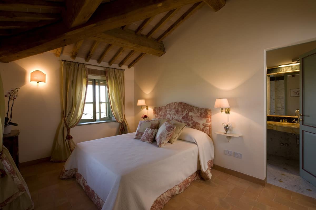 Een slaapkamer met een groot bed, twee bedlampen, een raam met gordijnen en een houten plafond.