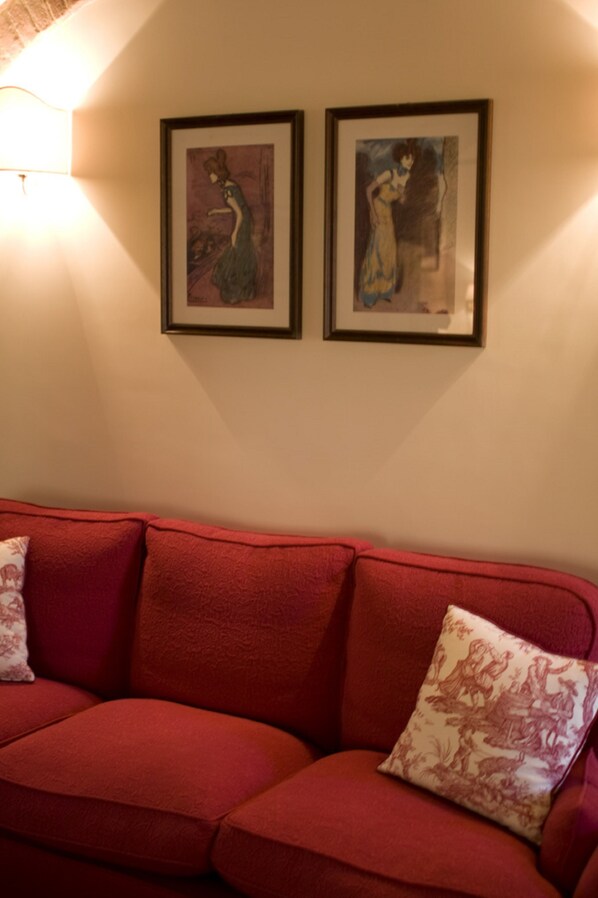 A red sofa with two cushions and two framed artworks on the wall above. - Villa Il Castagno Wine & Resort (Siena)