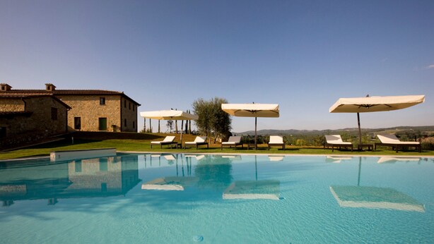 A swimming pool with lounge chairs and umbrellas, a stone building, and a clear sky. - Villa Il Castagno Wine & Resort (Siena)