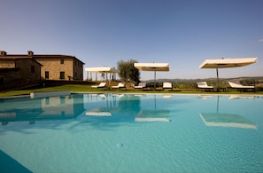 A swimming pool with lounge chairs and umbrellas, a stone building, and a clear sky. - Villa Il Castagno Wine & Resort (Siena)