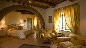 A bedroom with a bed, two armchairs, a small table, and a window with curtains. - Villa Il Castagno Wine & Resort (Siena)