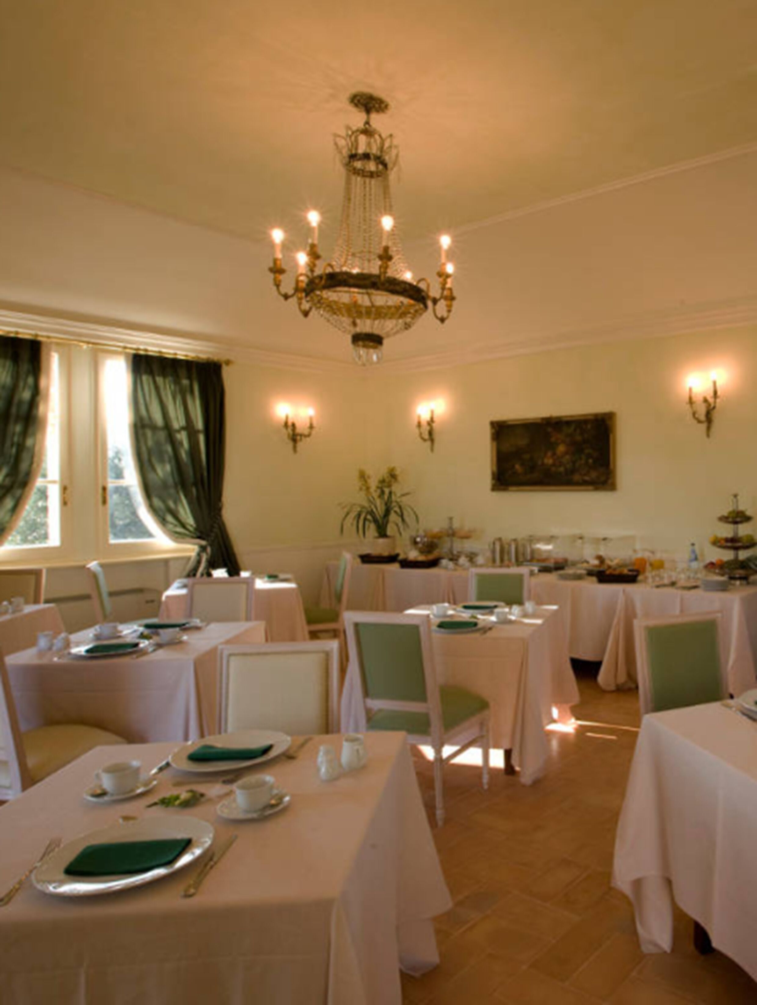 A dining area with tables set for service, a chandelier, and wall sconces.