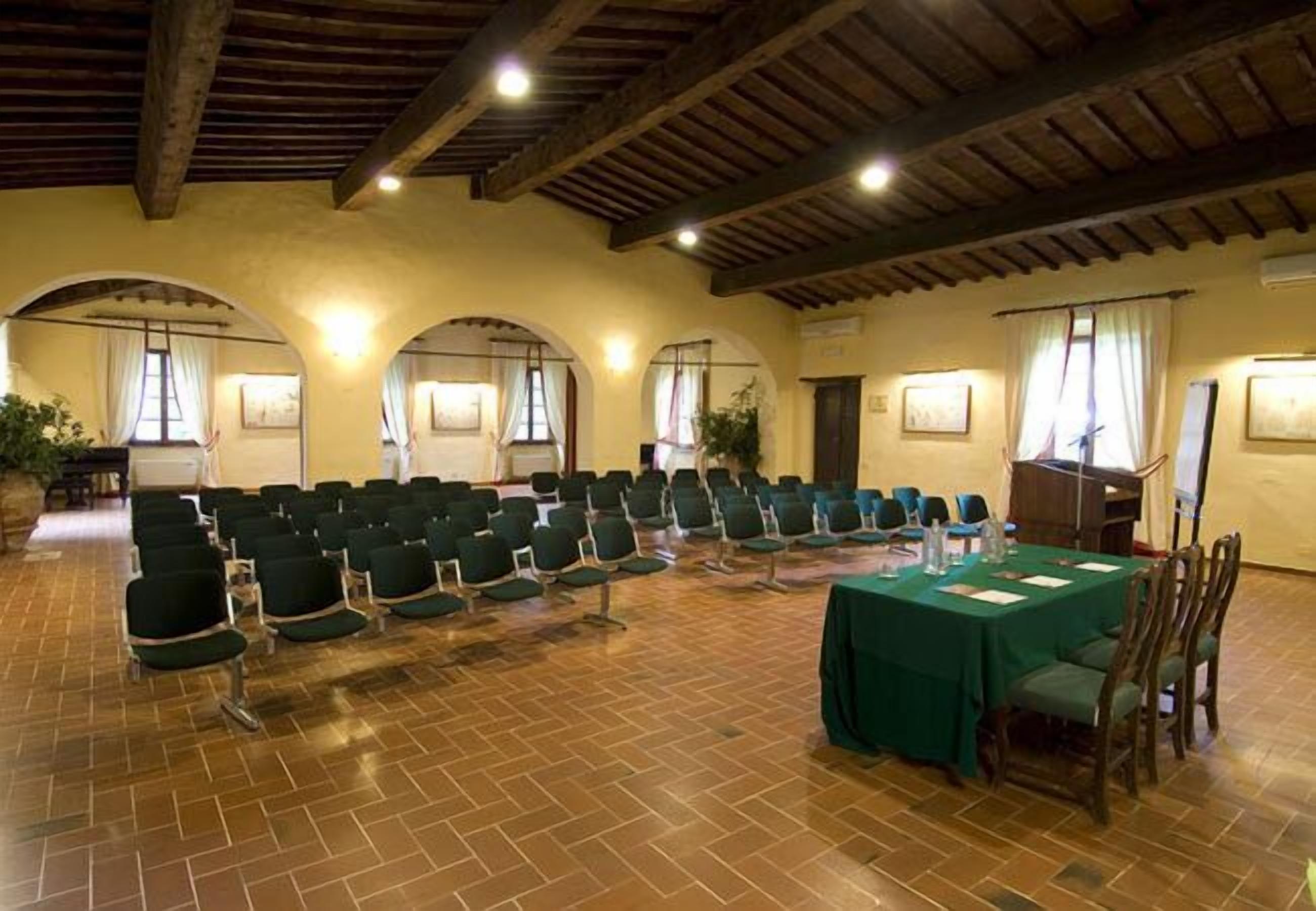 A conference room with rows of chairs, a table with a green tablecloth, and wooden beams on the ceiling.