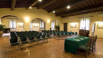 A conference room with rows of chairs, a table with a green tablecloth, and wooden beams on the ceiling.