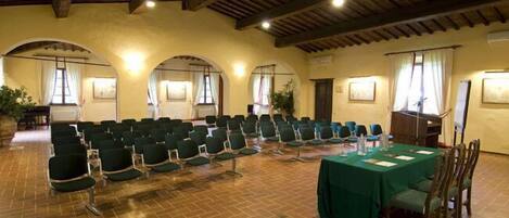A conference room with rows of chairs, a table with a green tablecloth, and wooden beams on the ceiling.
