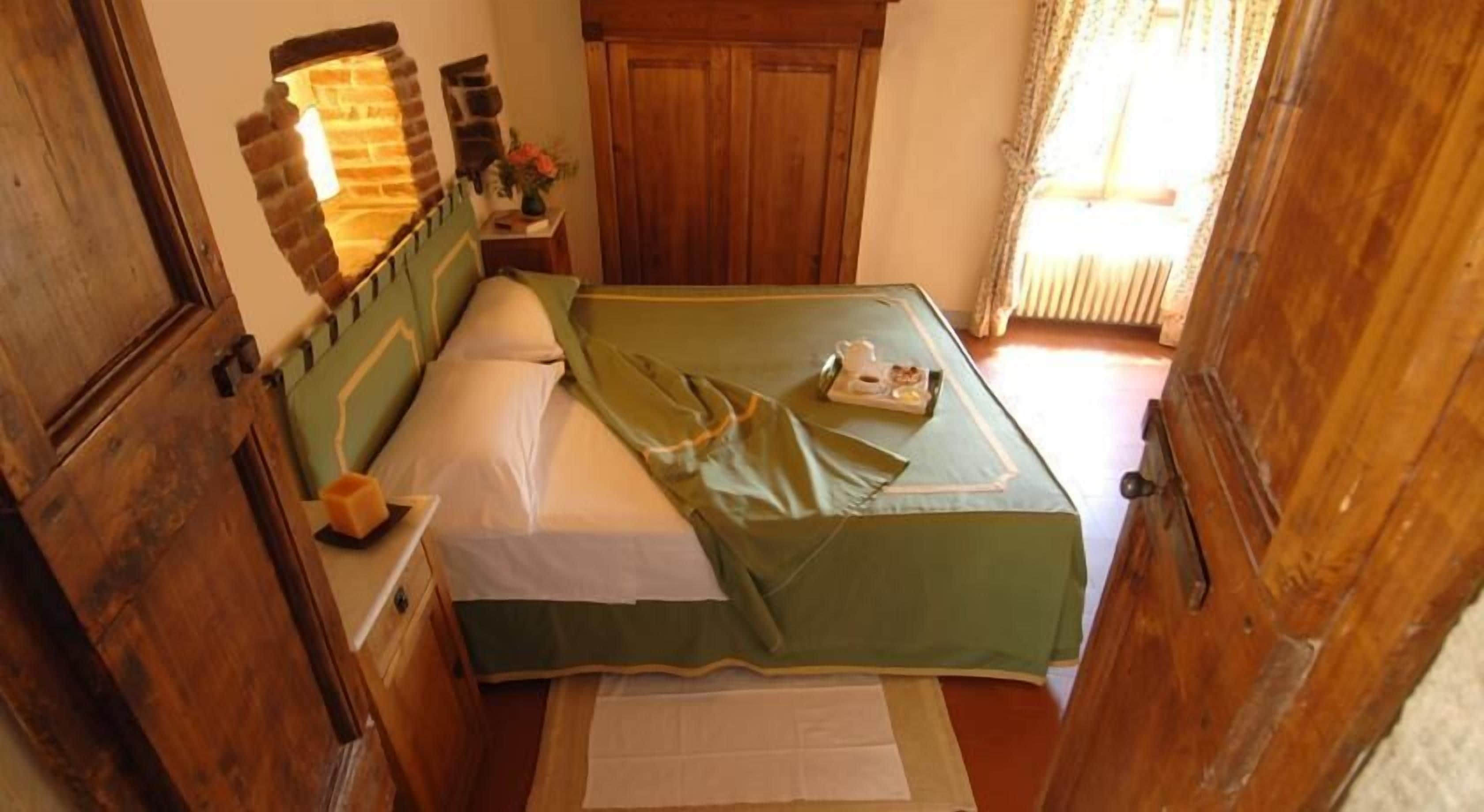 Una camera da letto piccola e accogliente con una coperta verde, una testiera in legno, un comodino con una lampada e una finestra con tende.