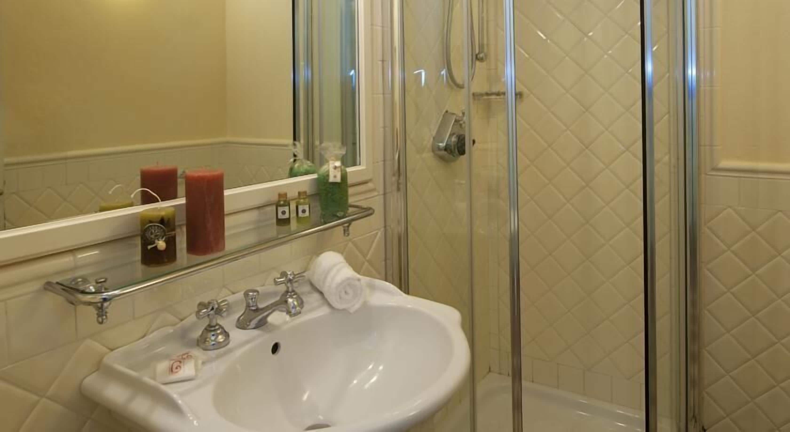 A bathroom with a white sink, a glass shower enclosure, and toiletries on a shelf.