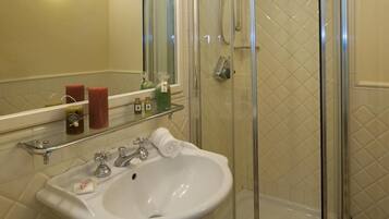 A bathroom with a white sink, a glass shower enclosure, and toiletries on a shelf.