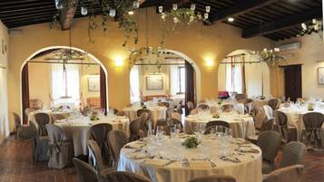 A dining area with round tables set for a meal, featuring a rustic ceiling with hanging plants and exposed beams.