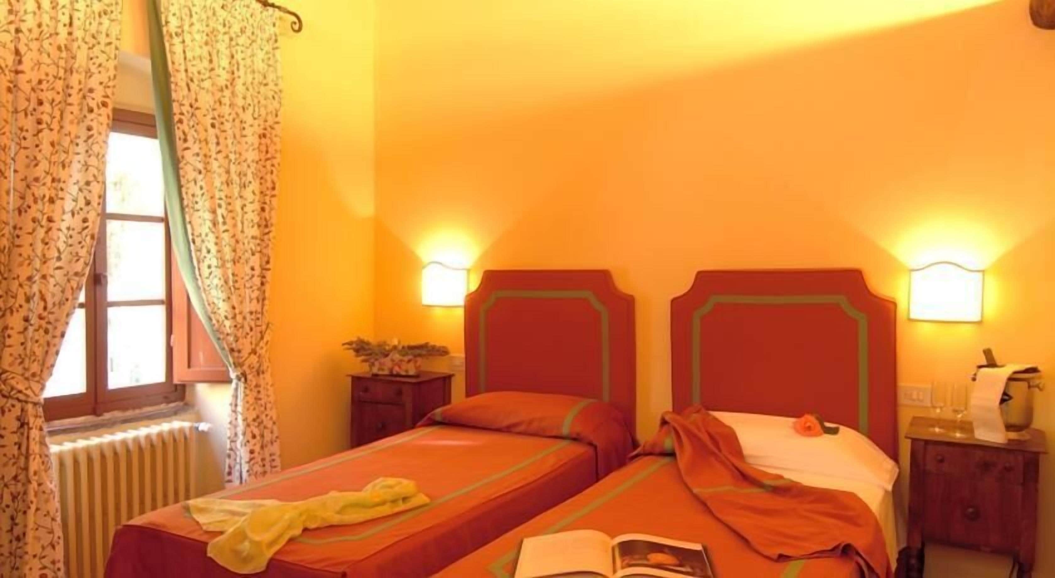 Quarto com duas camas, janela com cortinas, luminárias de cabeceira, radiador e uma pequena mesa com uma planta.