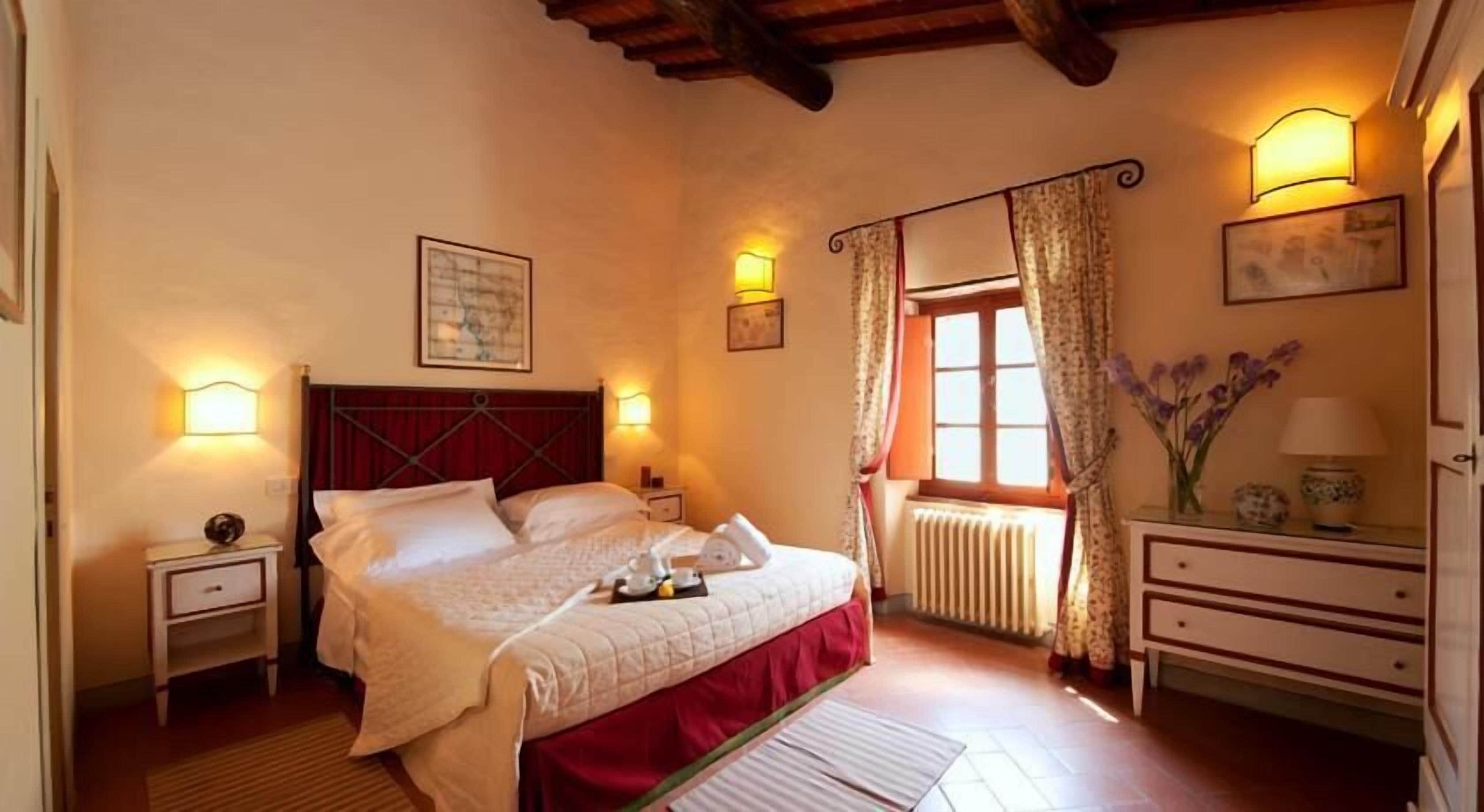 Une chambre à coucher comprenant un lit, des tables de chevet, un radiateur, une fenêtre avec des rideaux et des lampes fixées au mur.