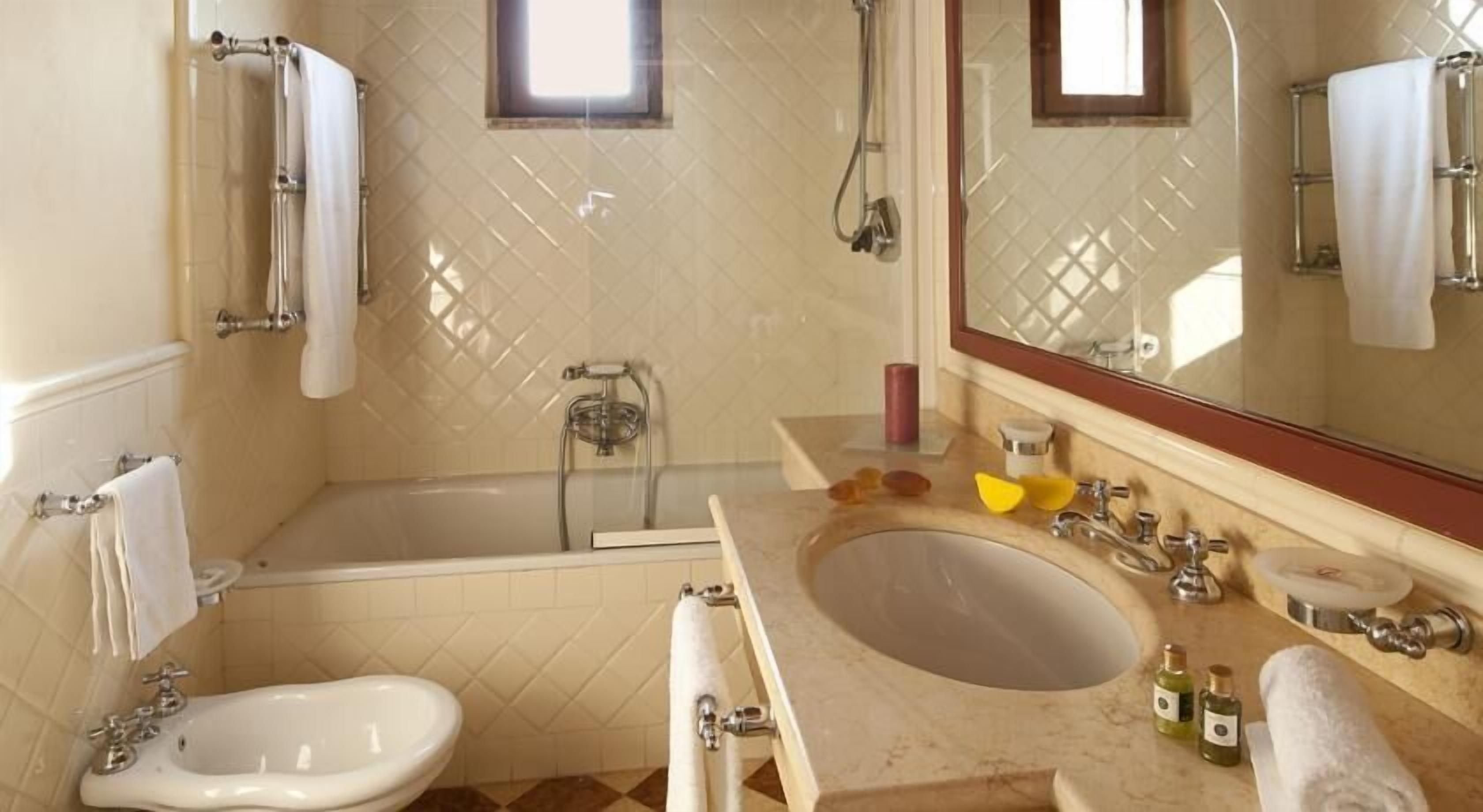 A bathroom with a bathtub, a sink, and a bidet. There is a window above the bathtub, and a mirror above the sink.