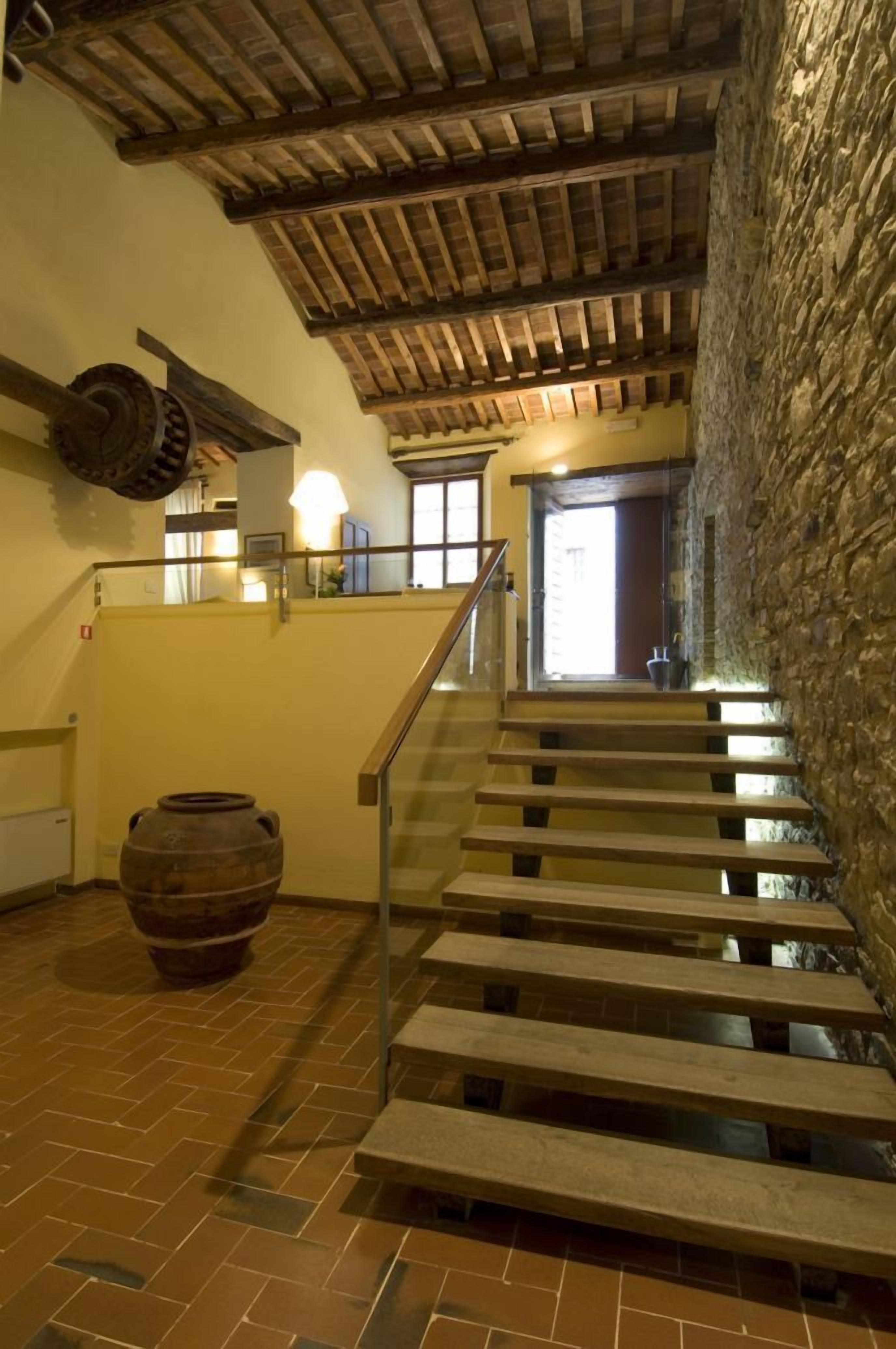 Un escalier avec des marches en bois et une rampe en métal, menant à un mur de pierre et à une fenêtre.