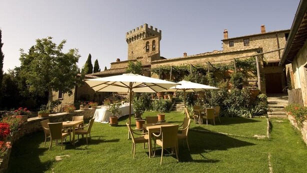 A courtyard with outdoor seating, a stone building with a tower, and a well-maintained garden. - Castello di Gargonza (Monte San Savino)