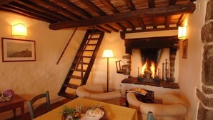 A cozy room with a fireplace, wooden beams, a ladder, and a table with a bowl of fruit. - Castello di Gargonza (Monte San Savino)