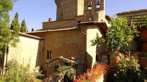 A historic stone building with a tower, surrounded by a well-maintained garden with flowering plants. - Castello di Gargonza (Monte San Savino)