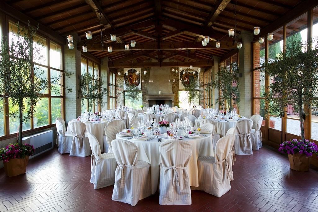 A banquet hall with round tables set for a formal event, large windows, and a rustic wooden ceiling.