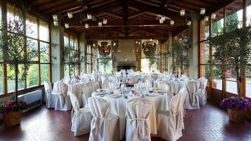 A banquet hall with round tables set for a formal event, large windows, and a rustic wooden ceiling.