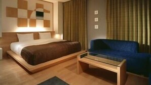 Une chambre d’hôtel avec un lit, un canapé bleu, une table basse en verre et un mur orné d’un motif géométrique.