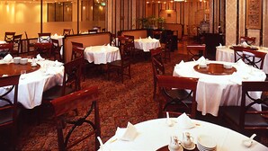 Un restaurant doté de nombreuses tables, chacune recouverte d’une nappe blanche et agrémentée de chaises, et dont le sol est recouvert d’un tapis.