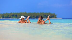 Dos personas descansando en agua turquesa cristalina con una isla boscosa al fondo.