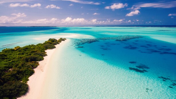 Una playa tropical con aguas turquesas cristalinas, una orilla de arena y vegetación verde exuberante.
