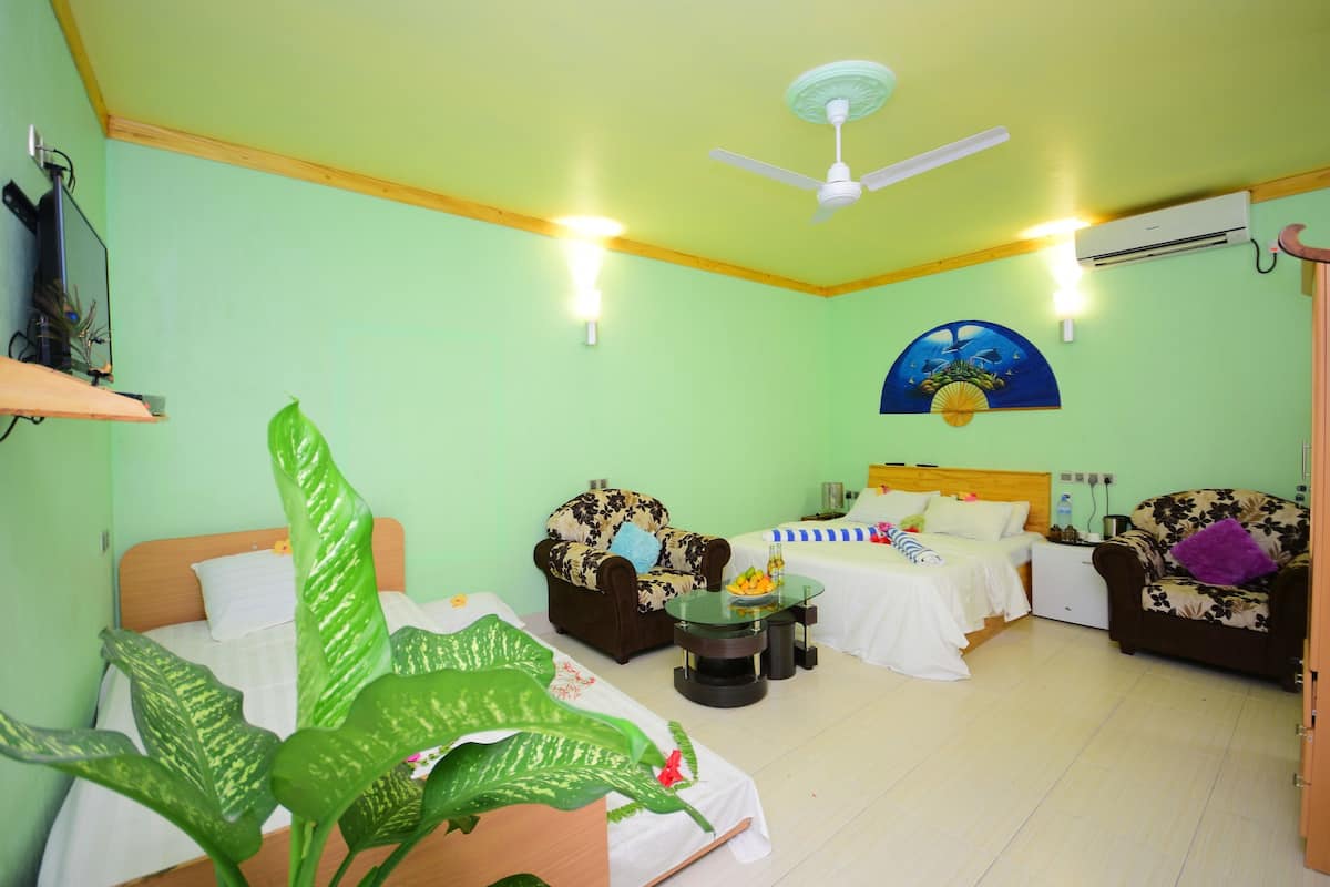 A room with a bed, two sofas, a small table, and a ceiling fan.