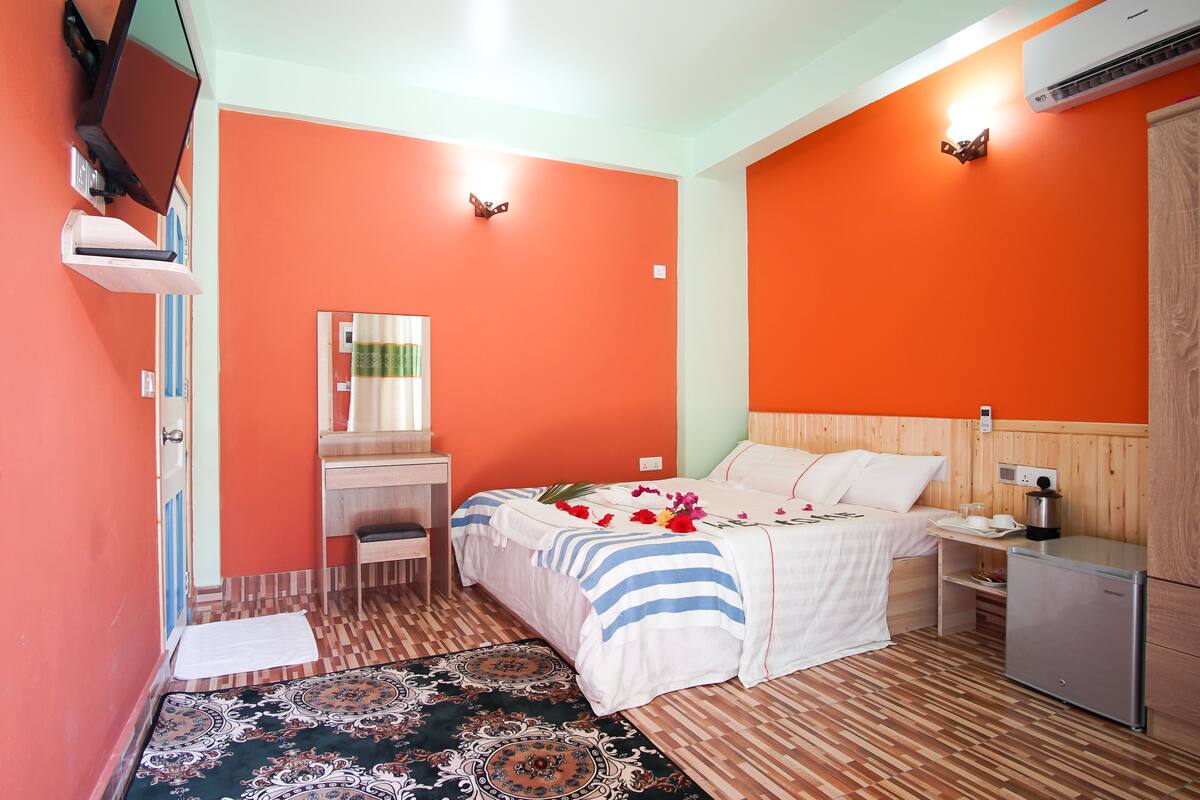 A hotel room with a bed, bedside table, desk, chair, and an air conditioning unit.
