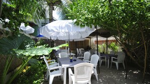 Un patio al aire libre con mesas y sillas de plástico blanco, cubierto por sombrillas blancas.