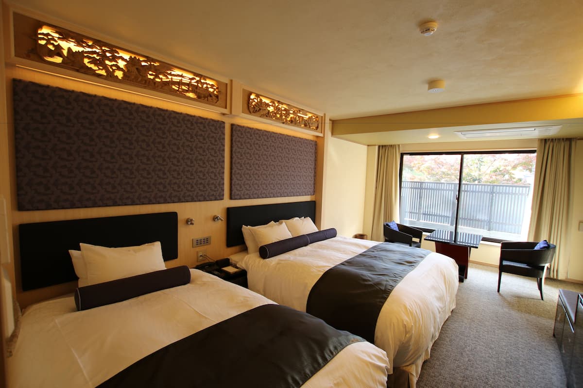 A hotel room with two beds, a desk, and a window with curtains.