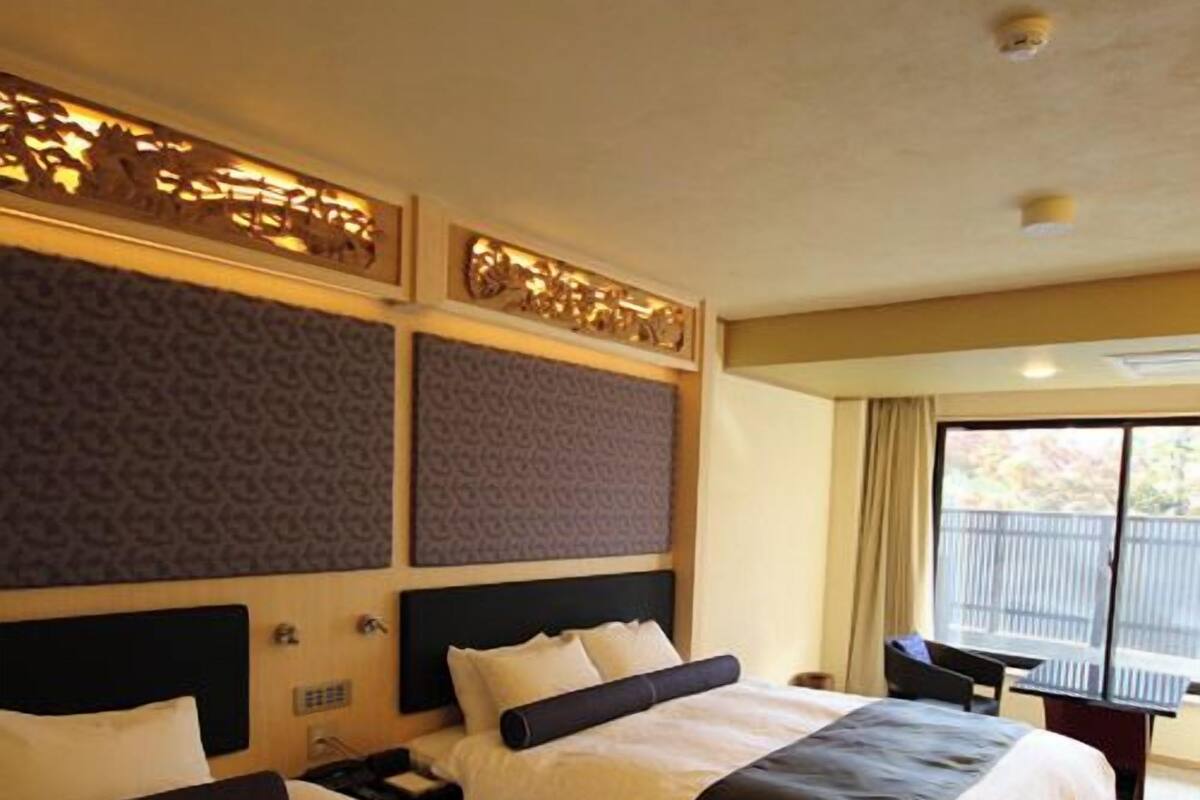 A hotel room with two beds, a desk, and a window with a view.