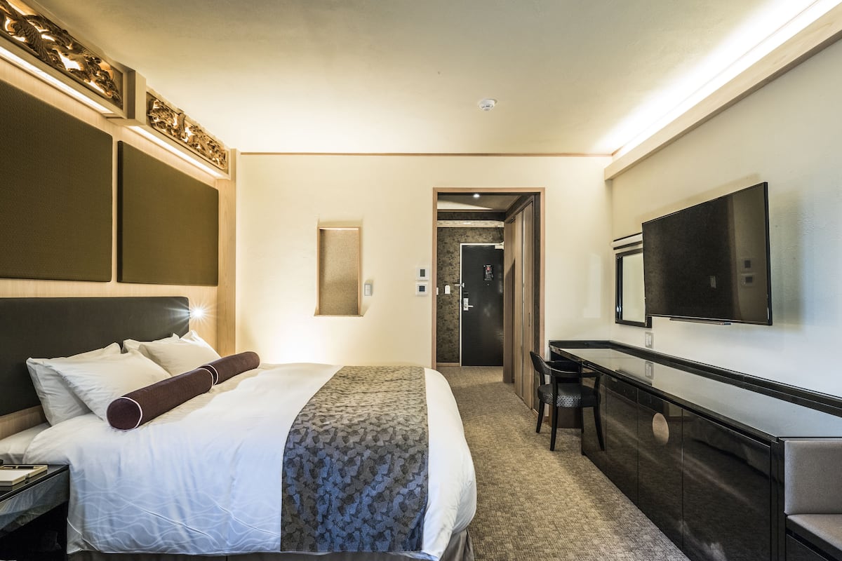 A hotel room with a large bed, a desk, a flat-screen TV, and a door leading to a bathroom.