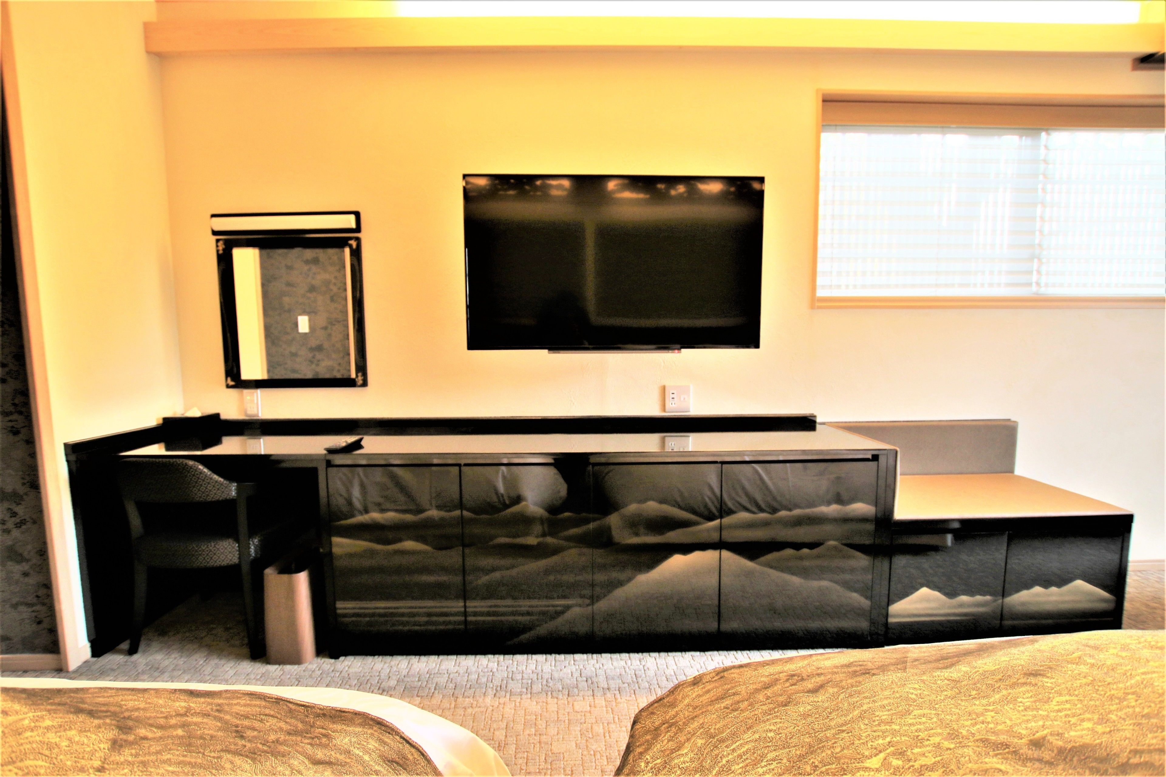 A hotel room with a sofa bed, a desk, a chair, a television, and a window with blinds.