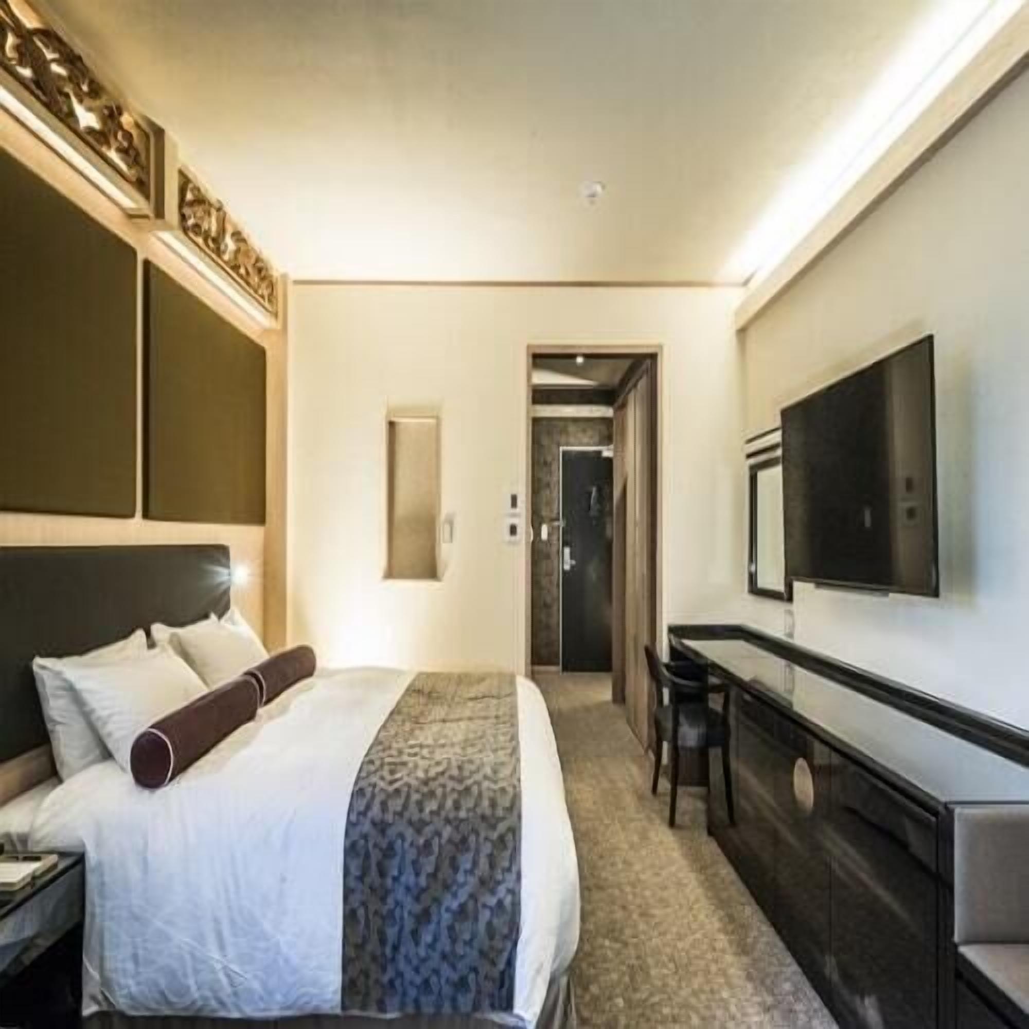 Ein Hotelzimmer mit einem Bett, einem Schreibtisch, einem Stuhl, einem Fernseher und einer Tür zu einem anderen Raum.