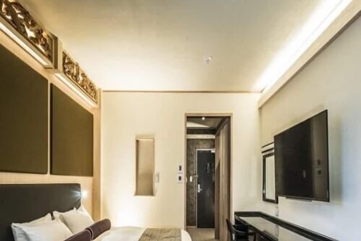 A hotel room with a bed, a desk, a chair, a television, and a door leading to another room.
