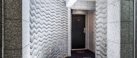 A narrow hallway with a patterned wall and a carpeted floor, leading to a door marked with the number 103.