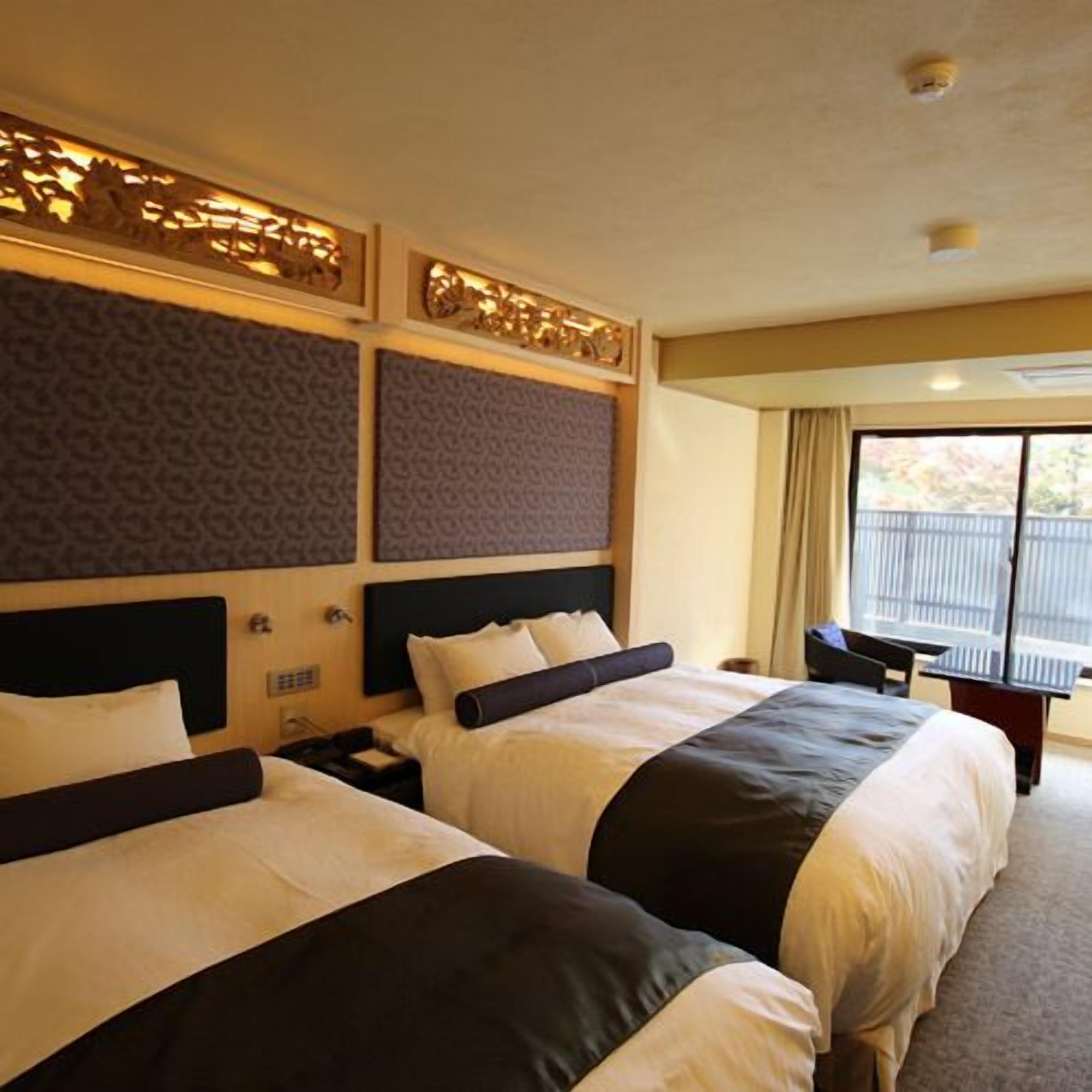 A hotel room with two beds, a desk, and a large window.