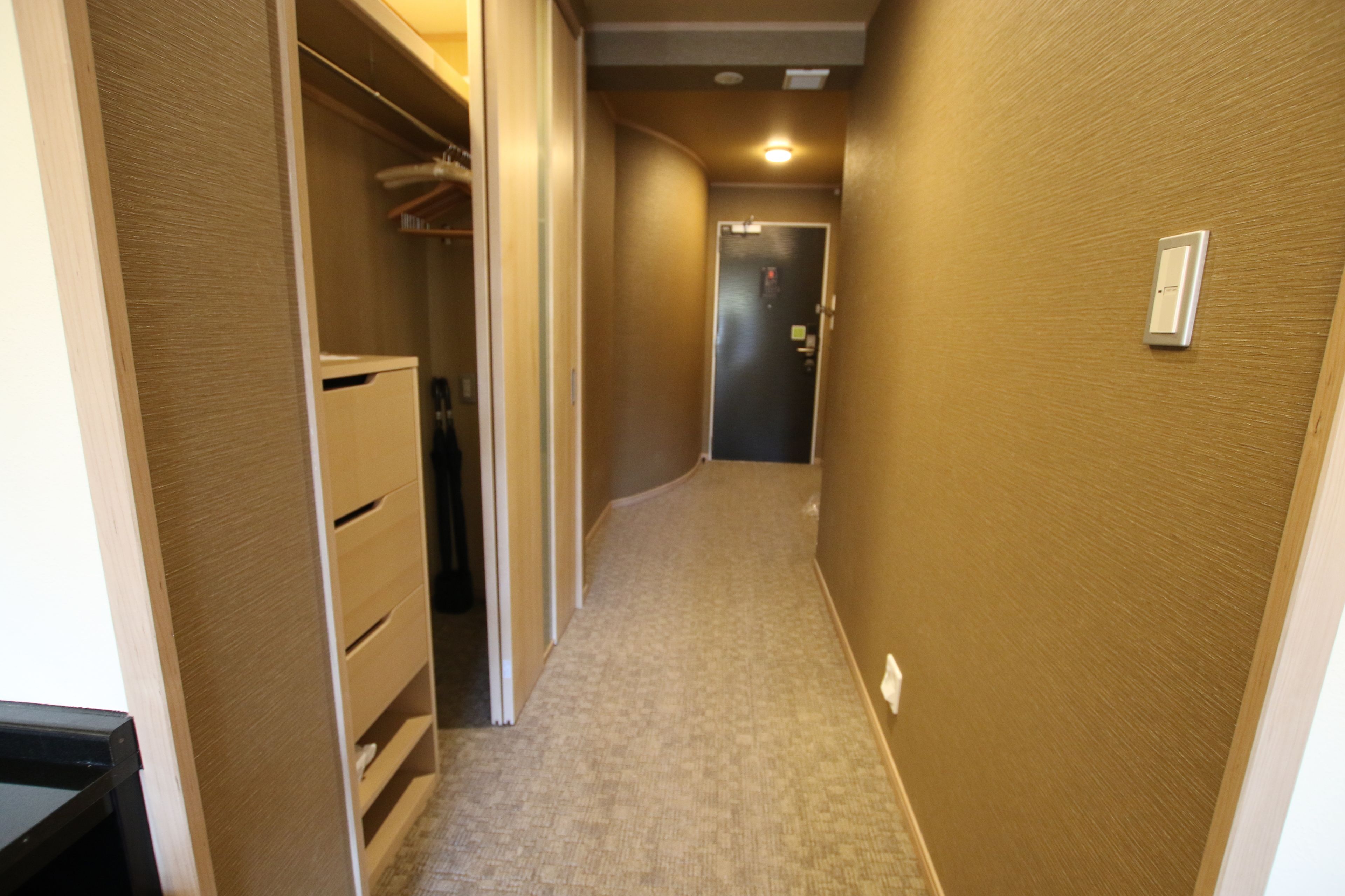 Un couloir étroit, doté d’un sol recouvert de moquette, de murs en bois et d’une porte au fond.