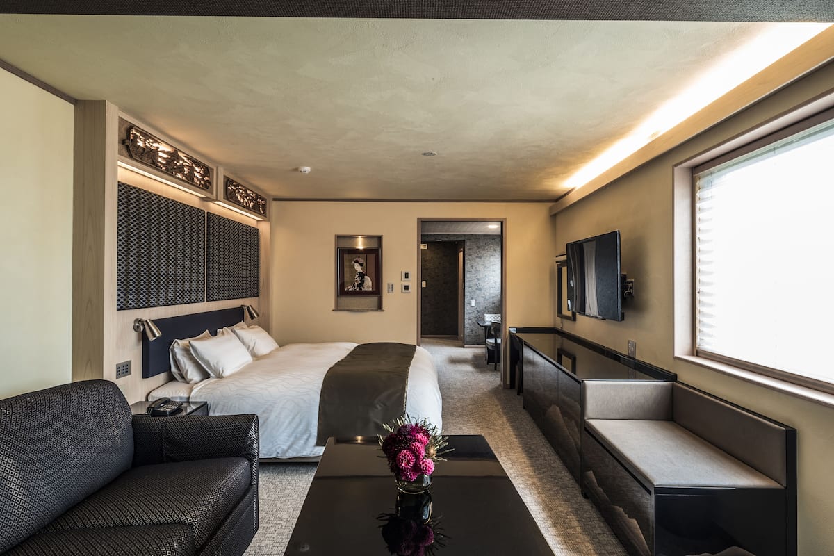 A modern hotel room with a large bed, a sofa, a coffee table with flowers, and a TV mounted on the wall.