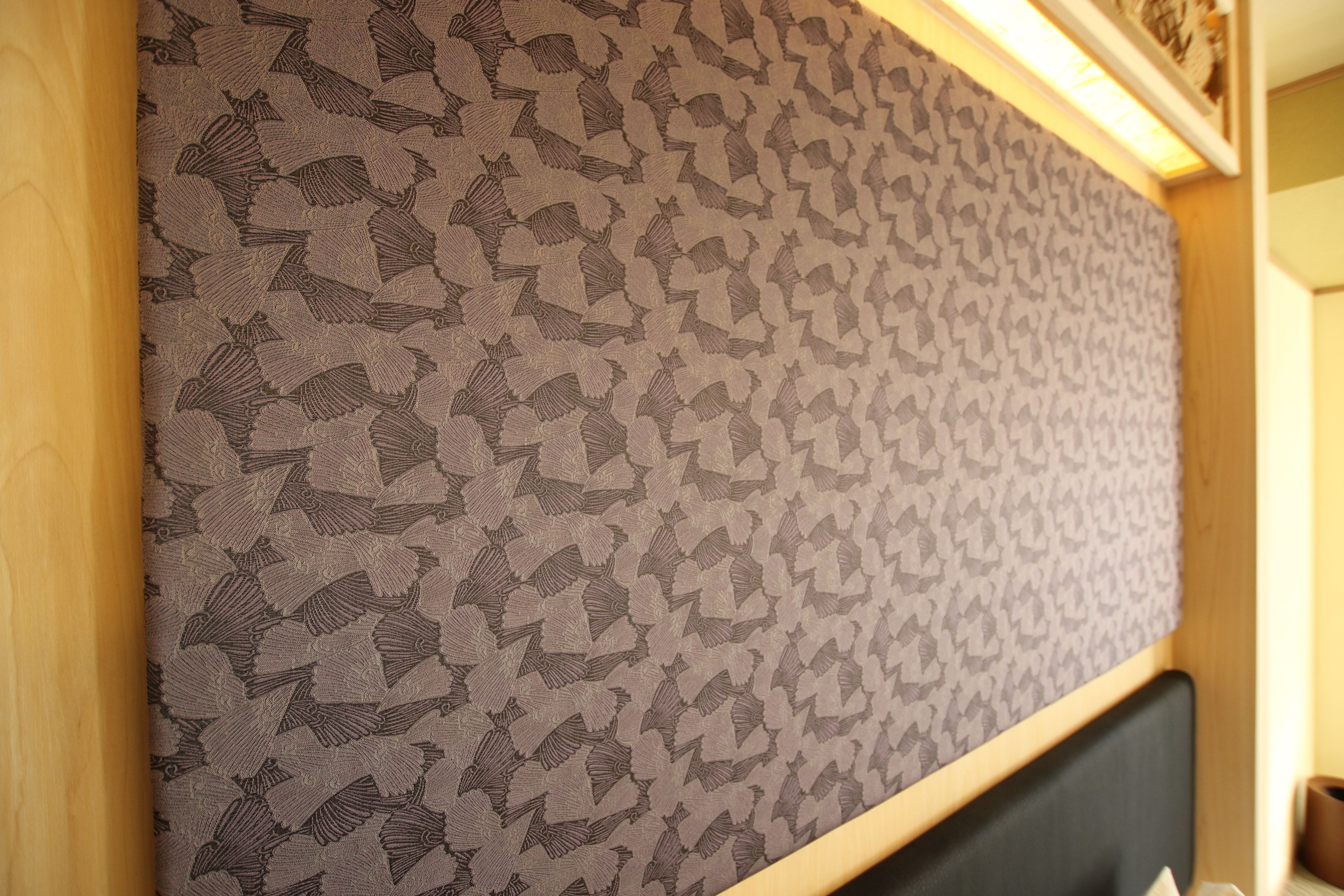 A wall with a patterned wallpaper featuring a repeated design.