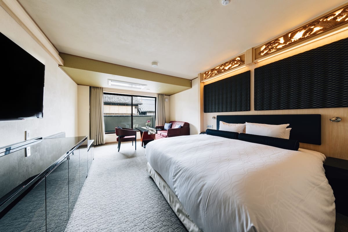 A hotel room with a large bed, a desk, a chair, and a television.