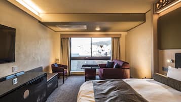 Habitación de hotel con cama, escritorio, silla, televisor y balcón con vistas.