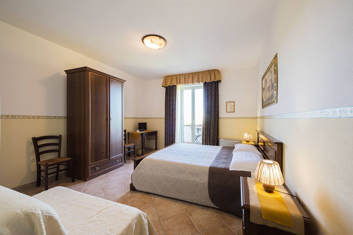 Ein Hotelzimmer mit zwei Betten, einem Schreibtisch, einem Stuhl, einem Kleiderschrank und einem Fenster mit Vorhängen.