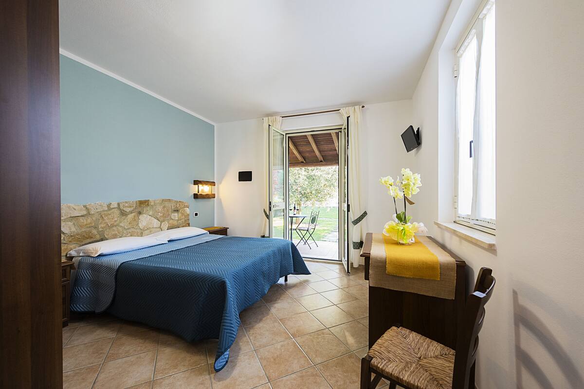 Ein Schlafzimmer mit einem Bett, einem kleinen Tisch mit gelber Tischdecke, einem Stuhl und einem Fenster mit Vorhängen.