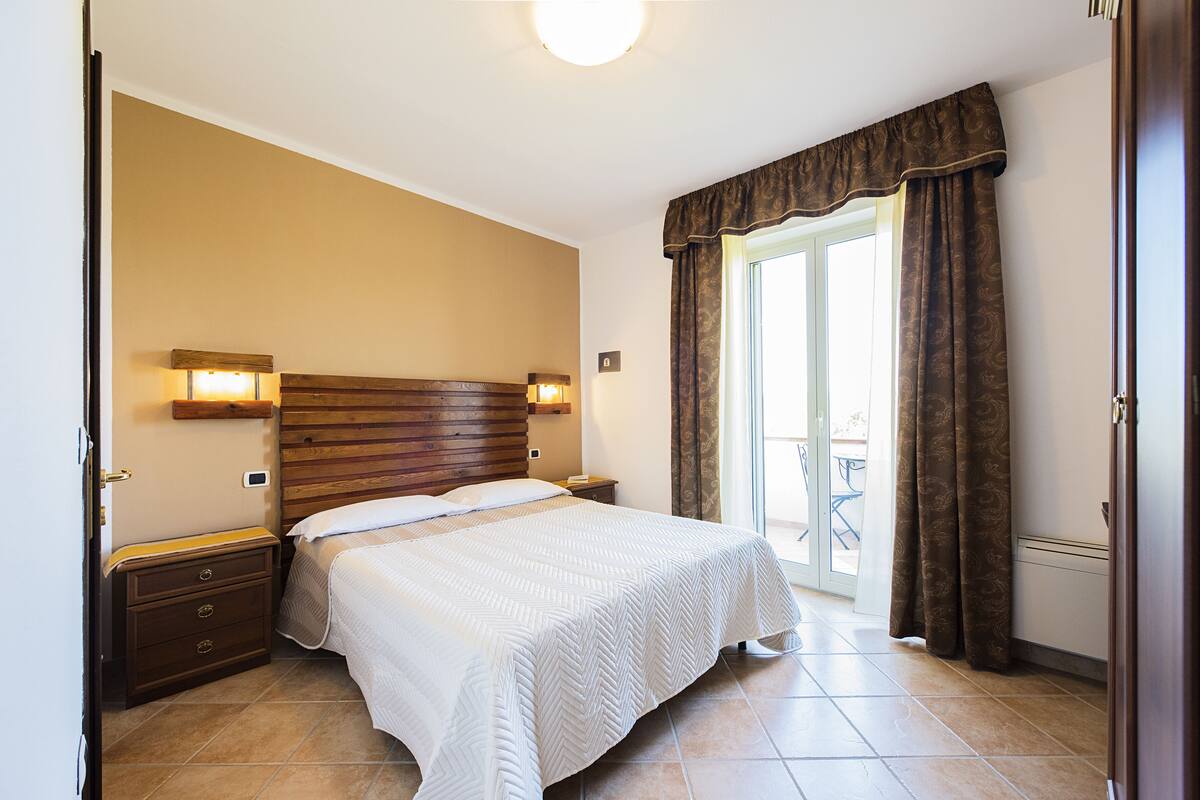 Ein Schlafzimmer mit Bett, Nachttischen, einem Holzkopfteil und einer Schiebetür zu einem Außenbereich.